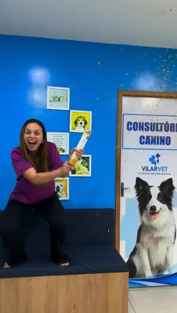 Integrante da equipe comemora com um lança-confetes em frente à parede azul, ao lado da porta do consultório canino.
